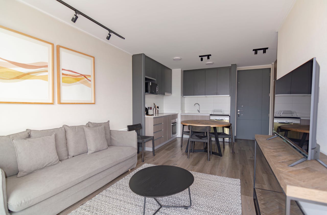 Contact Elegant modern living space with grey couch, minimalist decor, and open kitchenette.