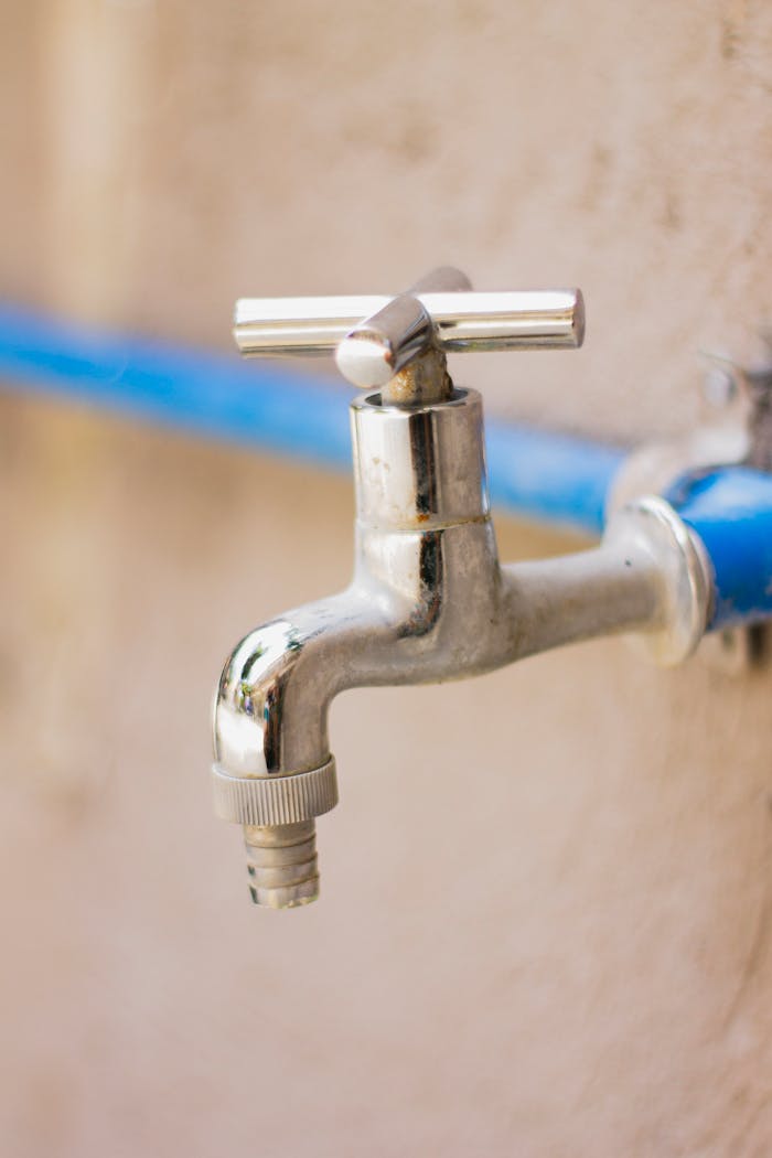Home A close-up view of a shiny stainless steel faucet attached to a blue pipe on a wall.